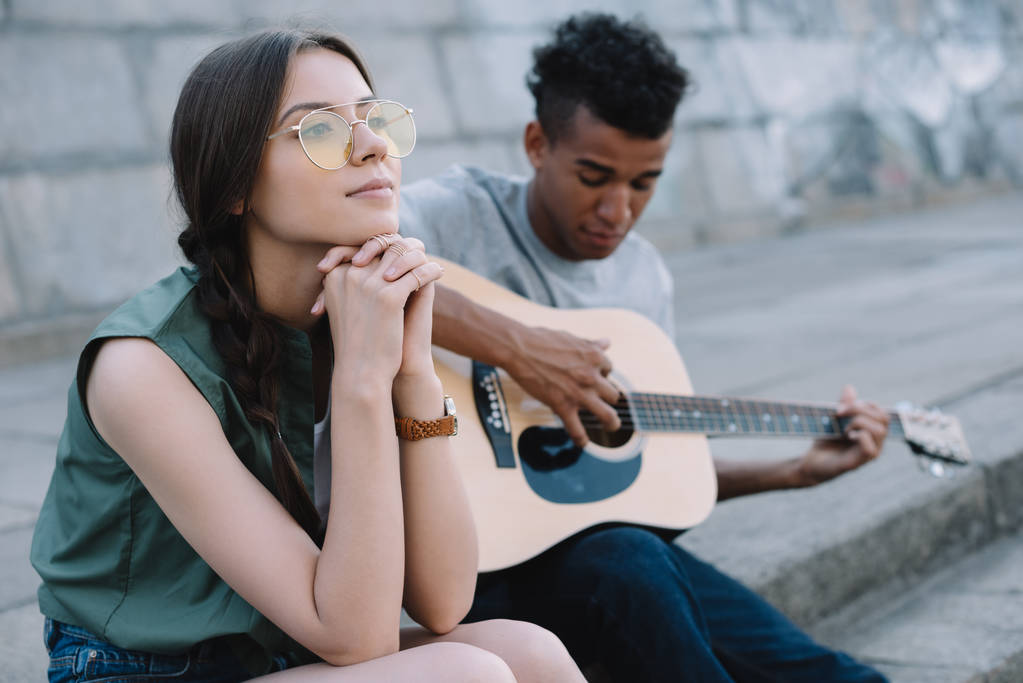 Chica soñadora escuchando al hombre afroamericano tocando la guitarra en la ciudad
 - Foto, imagen