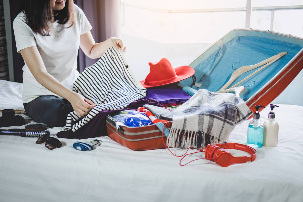 Concepto de viaje y vacaciones, felicidad mujer joven empacar una gran cantidad de su ropa y cosas en la maleta en la cama prepararse para el viaje y viaje en vacaciones
. - Foto, Imagen