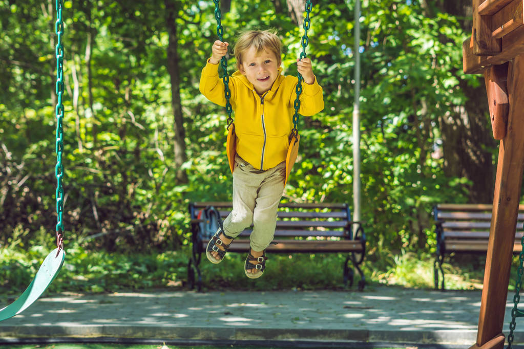 Menino em uma camisola amarela senta-se em um balanço em um playground no outono
. - Foto, Imagem