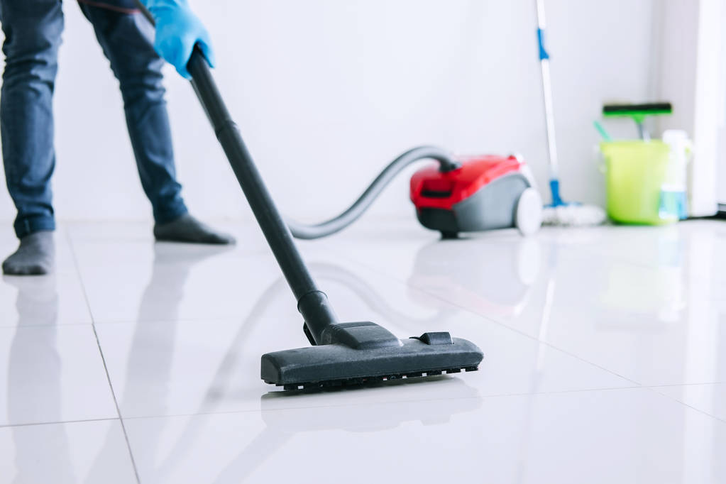 Housekeeping and housework cleaning concept, Happy young man in blue rubber gloves using a vacuum cleaner on floor at home. - Photo, Image