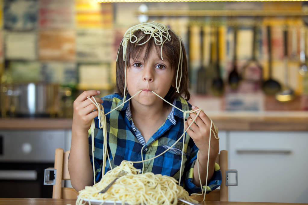 Menino pré-escolar, criança fofa, comer espaguete para o almoço e fazer uma casa de bagunça na cozinha
 - Foto, Imagem