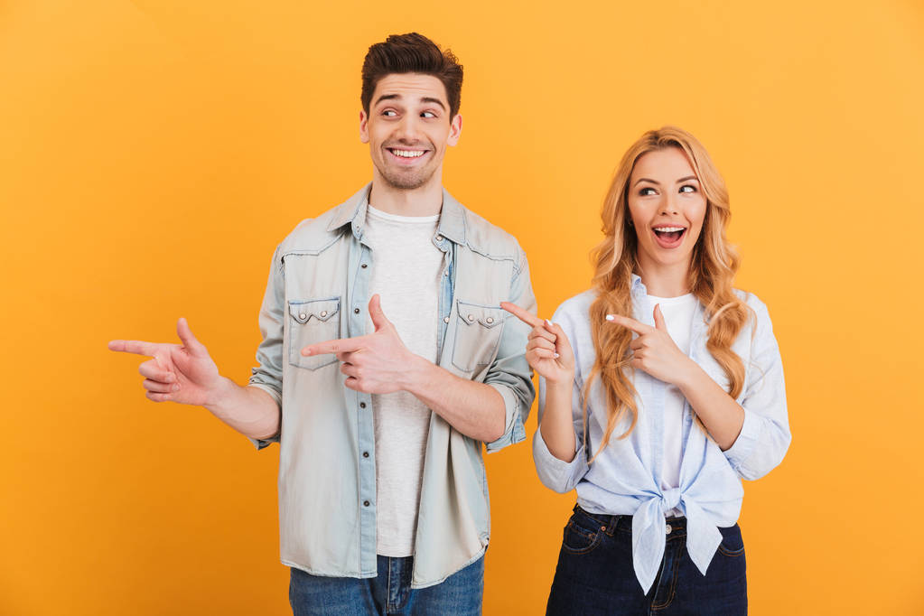 Foto von glücklichen Männern und Frauen in einfachen Kleidern, die lächeln und mit dem Finger zur Seite auf Kopierraum zeigen, der auf gelbem Hintergrund isoliert ist - Foto, Bild