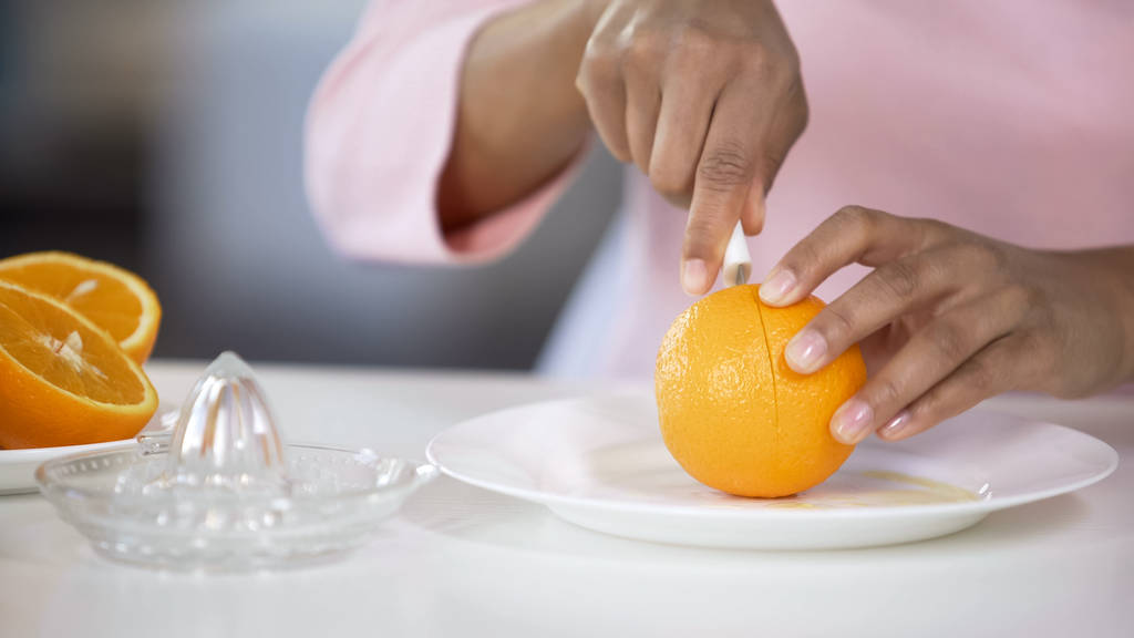 Многорасовая женщина режет оранжевый с ножом на тарелке, здоровое питание, витамины
 - Фото, изображение