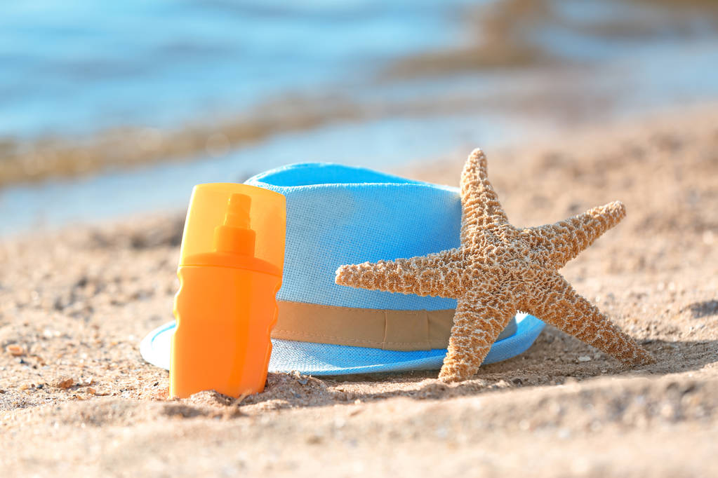 Starfish, bottle with sunscreen and hat on sand near sea. Beach object - Photo, Image