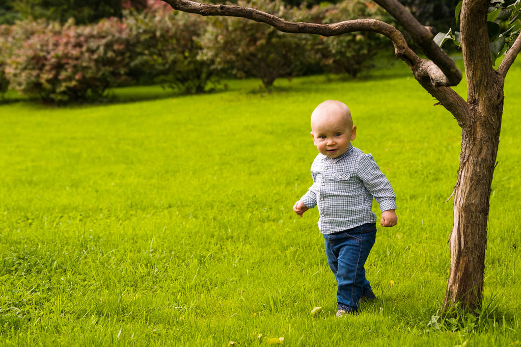 glimlachend jongetje wandelen op groen gras in jeans en shirt - Foto, afbeelding