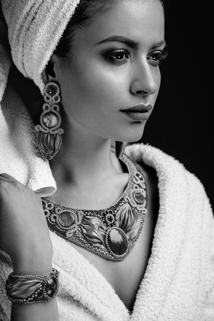 Mujer joven con albornoz y toalla en la cabeza, joyas de moda, spa y retrato de cuidado, cara natural limpia, retrato sobre un fondo oscuro
 - Foto, imagen