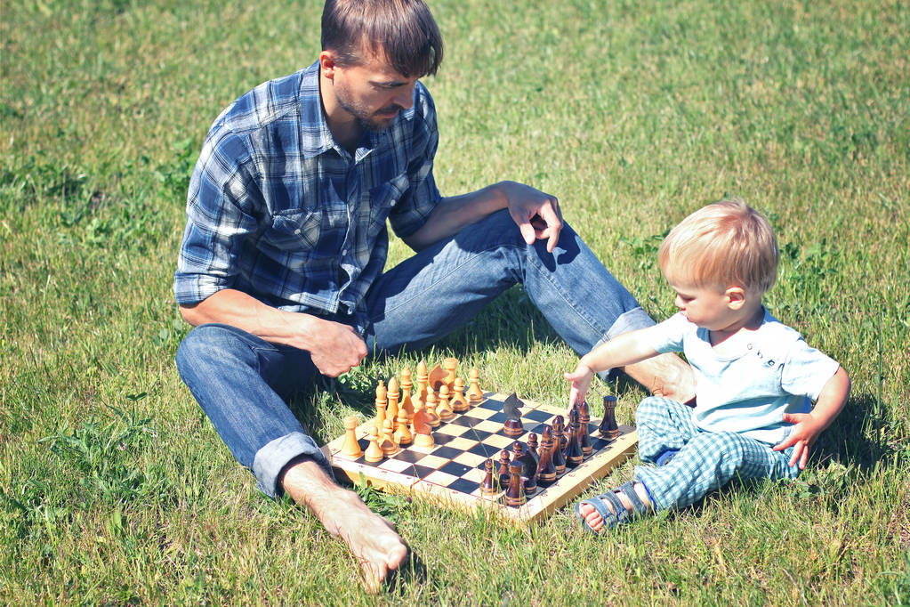 Papà insegna a suo figlio a giocare a scacchi. Papà e figlio tempo insieme all'aperto
. - Foto, immagini