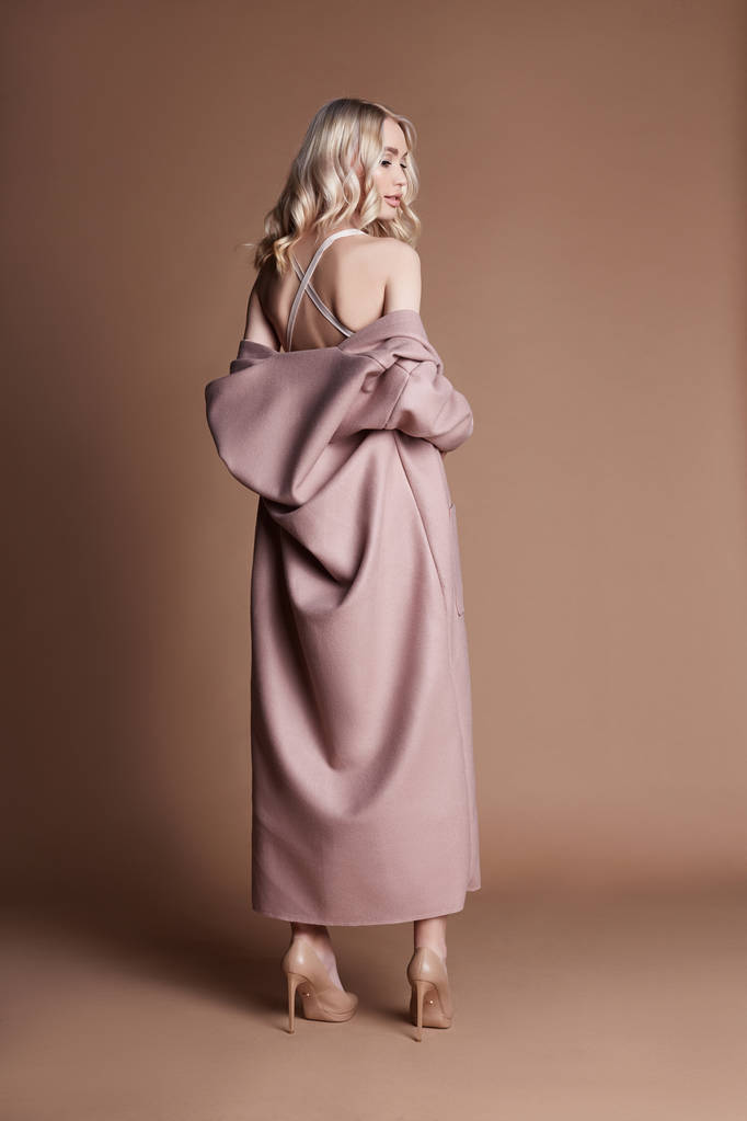 Mulher loira bonita posando em um casaco rosa em um fundo bege. Roupa de desfile de moda, mulher com figura perfeita, cabelo longo. Casaco de outono na moda na moda no corpo da menina
 - Foto, Imagem