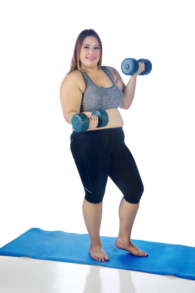 Ritratto di bella donna grassa che sorride alla telecamera mentre fa un allenamento con due manubri, isolata su sfondo bianco
 - Foto, immagini