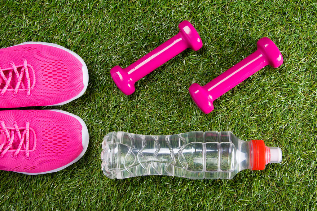 rosa Turnschuhe und Kurzhanteln für Fitness und eine Flasche Wasser vor dem Hintergrund von Gras - Foto, Bild