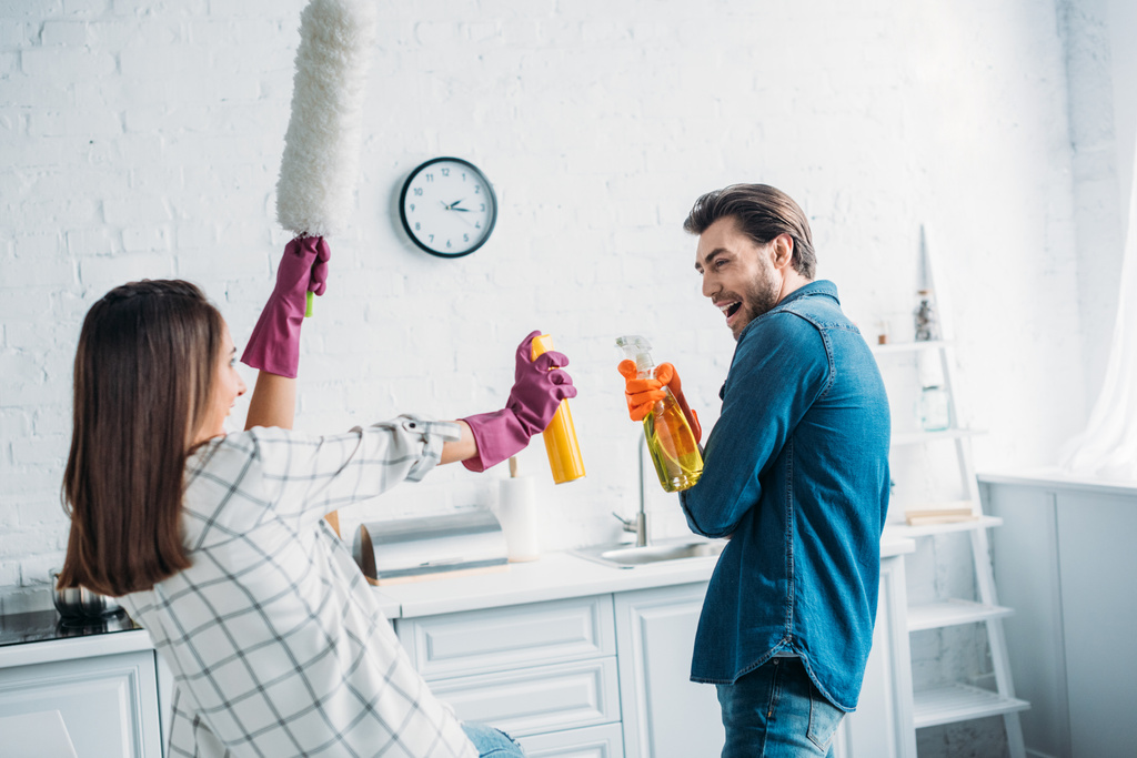 ευτυχισμένο ζευγάρι έχει τη διασκέδαση κατά τη διάρκεια καθαρισμού κουζίνας και αγωνίζονται με εργαλεία καθαρισμού - Φωτογραφία, εικόνα