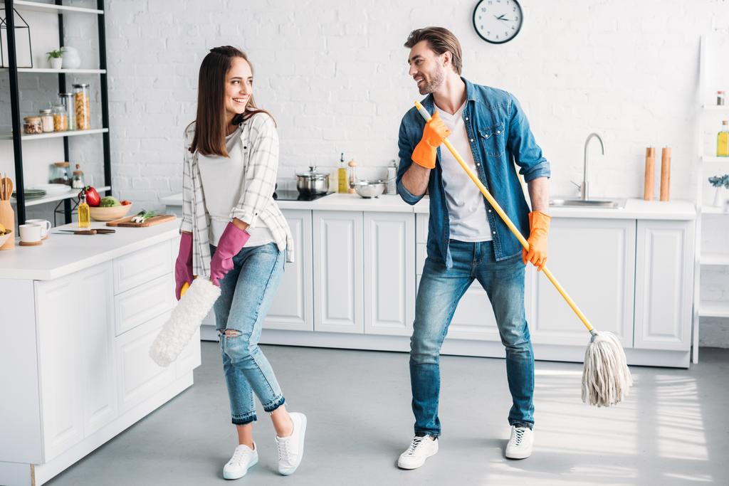 feliz novia y novio en guantes de goma divertirse con fregona en la cocina
 - Foto, Imagen