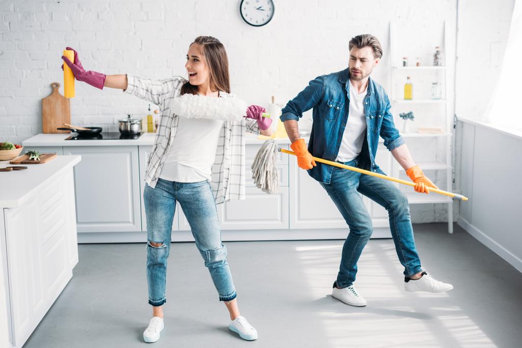 girlfriend and boyfriend in rubber gloves having fun with mop in kitchen - Photo, Image
