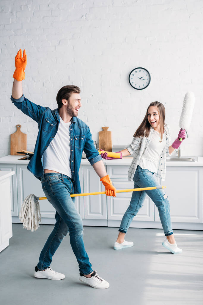 couple dans des gants en caoutchouc s'amuser avec balai et brosse à poussière dans la cuisine
 - Photo, image
