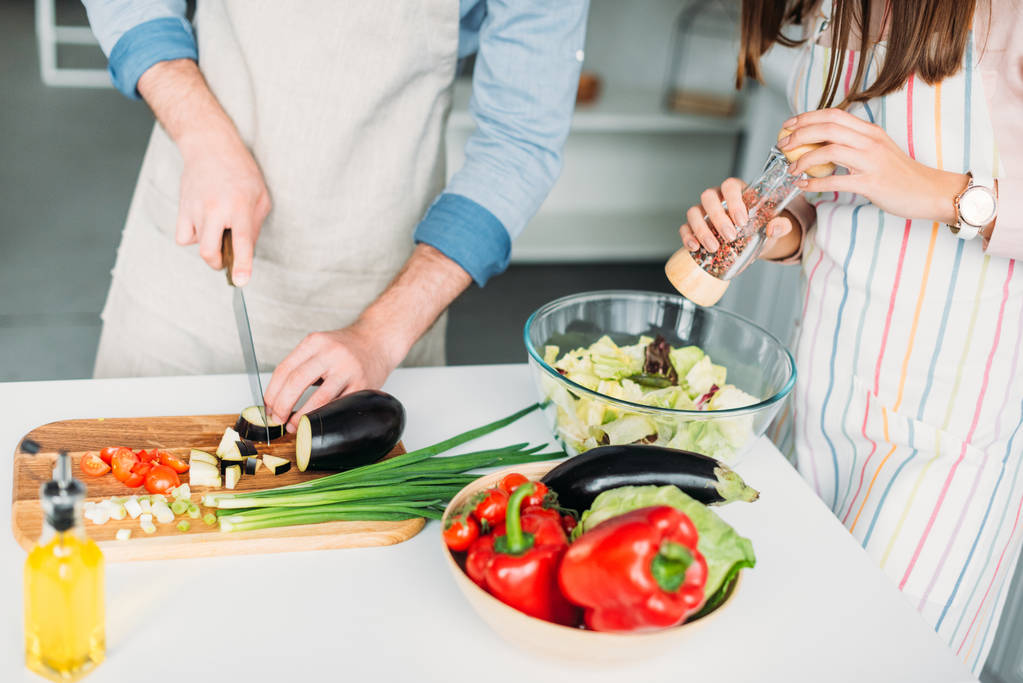 обрезанный образ бойфренда резки овощей и подруги добавления специй к салату на кухне
 - Фото, изображение