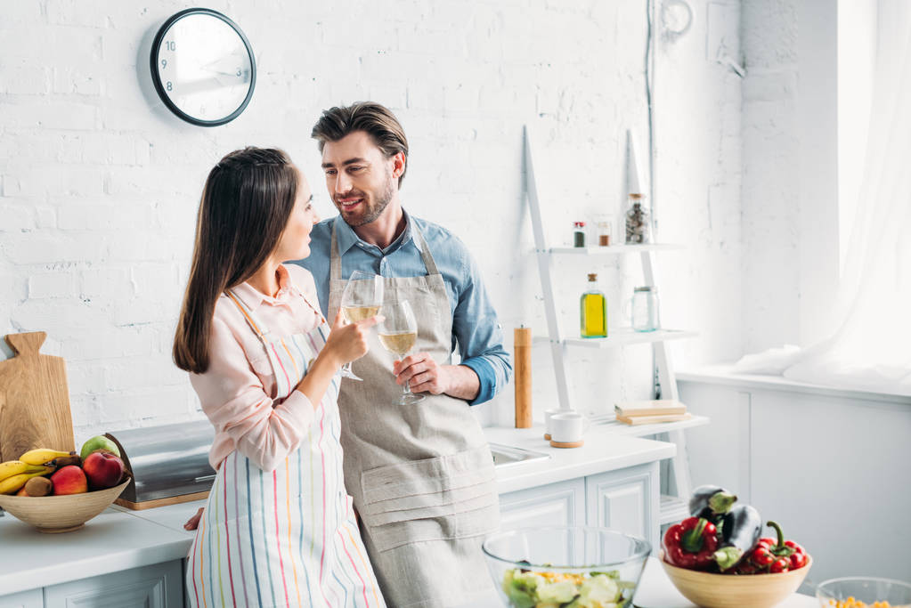boyfriend and girlfriend clinking with wineglasses in kitchen - Photo, Image