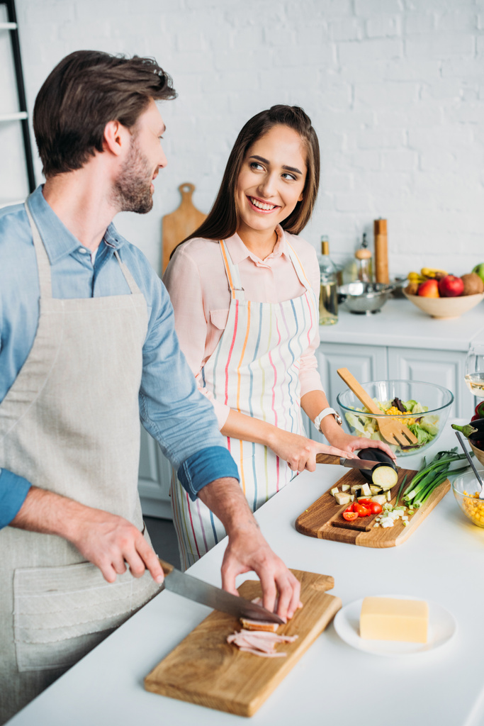 coppia sorridente che cucina e taglia verdure con carne in cucina
 - Foto, immagini