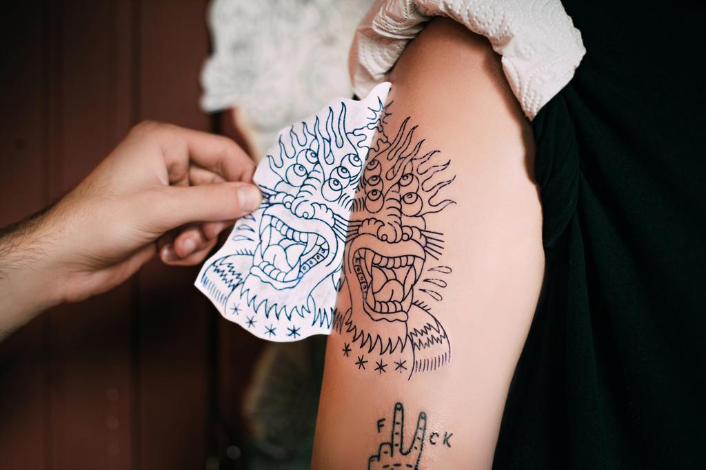 colpo ritagliato dell'artista del tatuaggio che trasferisce lo schizzo del tatuaggio sulla spalla nel salone del tatuaggio
  - Foto, immagini