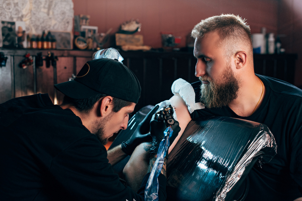 boční pohled na tetování umělce v rukavice pracují na tetování na rameni v salonu - Fotografie, Obrázek