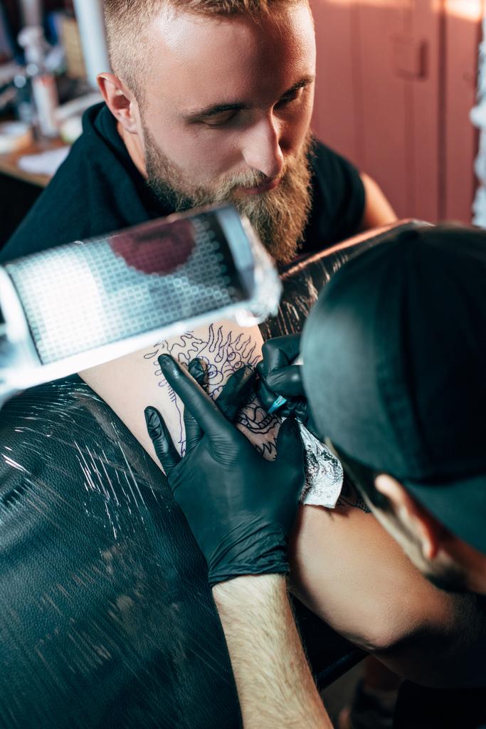fuoco selettivo dell'artista del tatuaggio nei guanti con macchina del tatuaggio che lavora sul tatuaggio sulla spalla nel salone
 - Foto, immagini