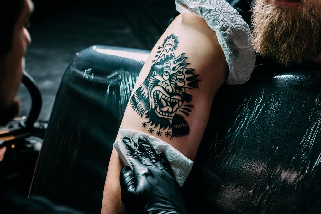 visão parcial do tatuador em luvas trabalhando na tatuagem no ombro no salão
 - Foto, Imagem