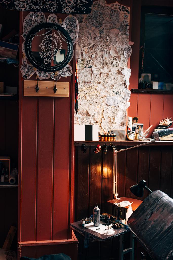 vista de perto de esboços na parede, máquinas de tatuagem arranjadas e pintura no salão de tatuagem
 - Foto, Imagem