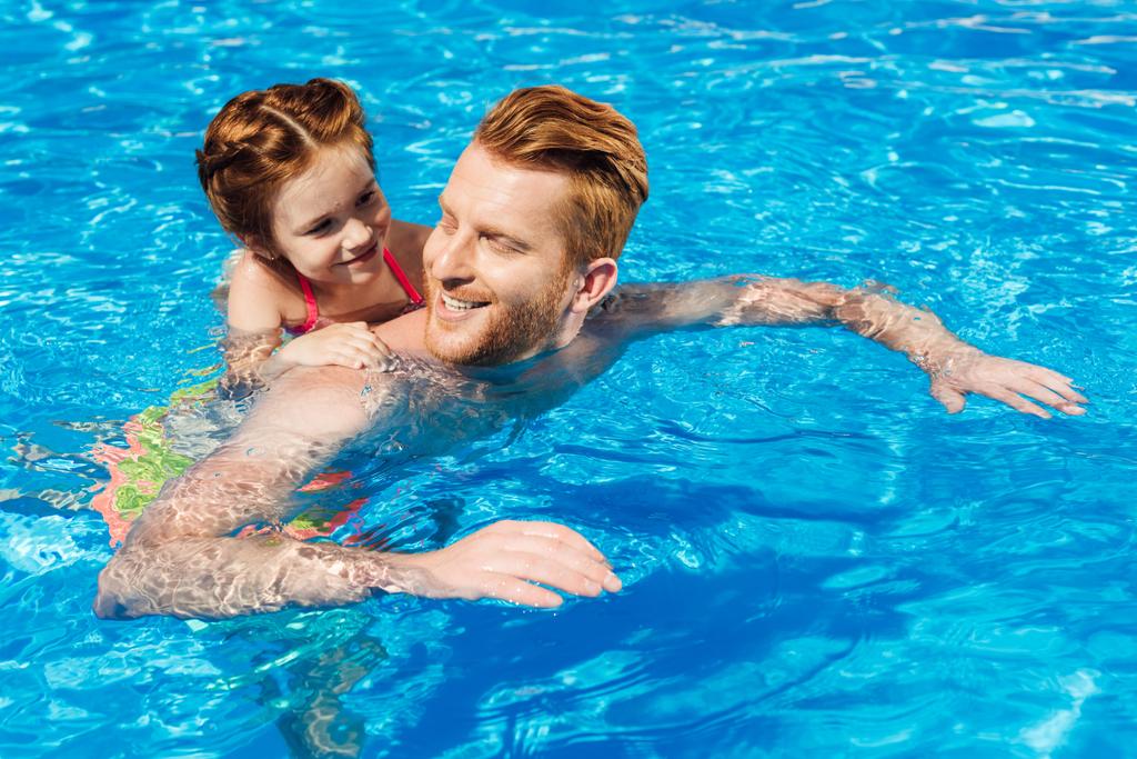 knappe blij vader zwemmen in zwembad en rit te geven aan dochter - Foto, afbeelding