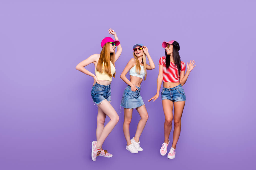 Ganzkörperporträt eines fröhlichen närrischen Trios in Jeans-Shorts Rock-Turnschuhen, das den gemeinsamen Urlaub isoliert auf leuchtend violettem Hintergrund genießt - Foto, Bild