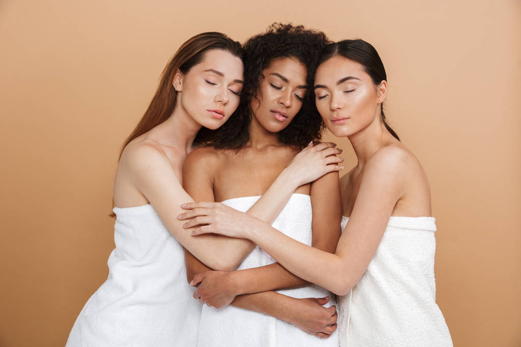 Три чувственные женщины, одетые в полотенца, позируют вместе с закрытыми глазами на бежевом фоне
 - Фото, изображение