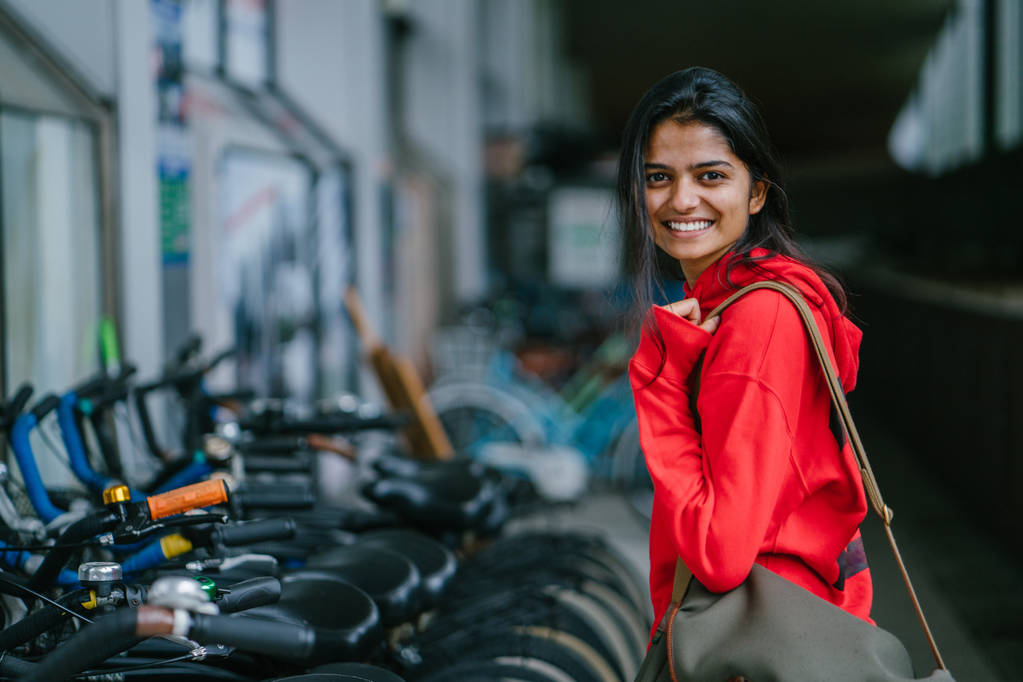retrato de chica india sonriente de pie sobre fondo con bicicletas estacionadas
 - Foto, Imagen
