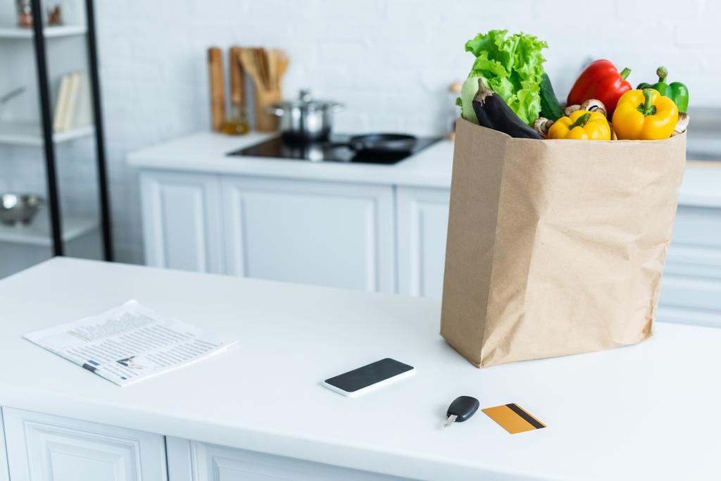 kruidenier zak, smartphone, krant, sleutel en creditcard op keukentafel - Foto, afbeelding
