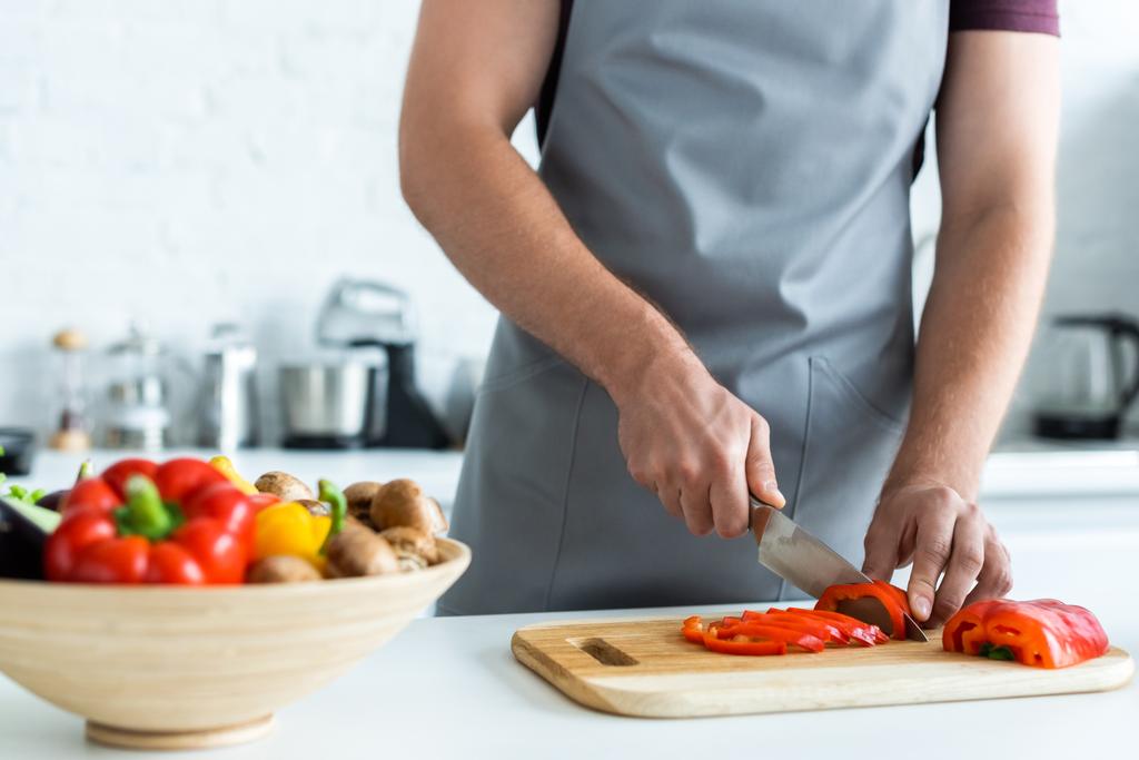 обрізаний знімок людини в фартусі, що ріже овочі на кухні
 - Фото, зображення