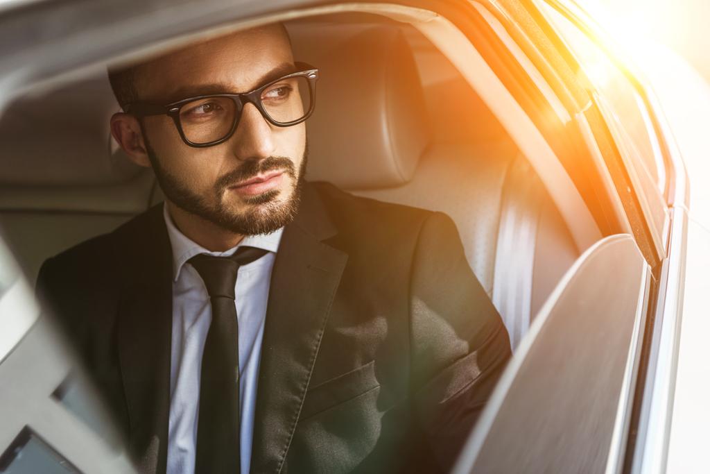 hombre de negocios guapo sentado en el coche y mirando hacia otro lado durante el atardecer
 - Foto, imagen