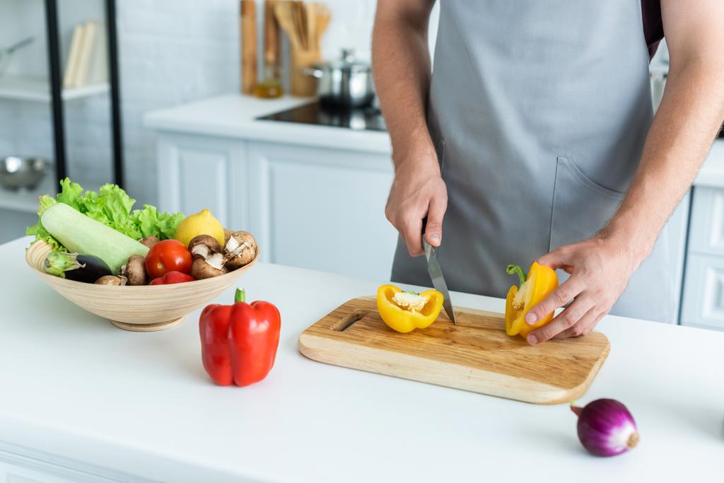 cropped shot of man in apron cutting bell pepper on wooden cutting board - Photo, Image