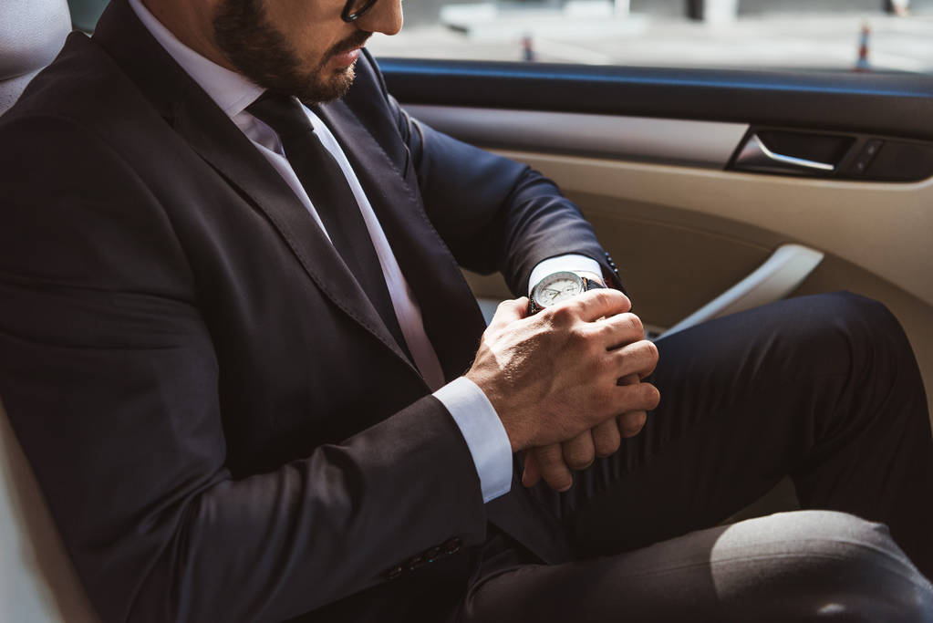 abgeschnittenes Bild eines Geschäftsmannes im Anzug, der die Uhrzeit auf einer Armbanduhr im Auto überprüft - Foto, Bild