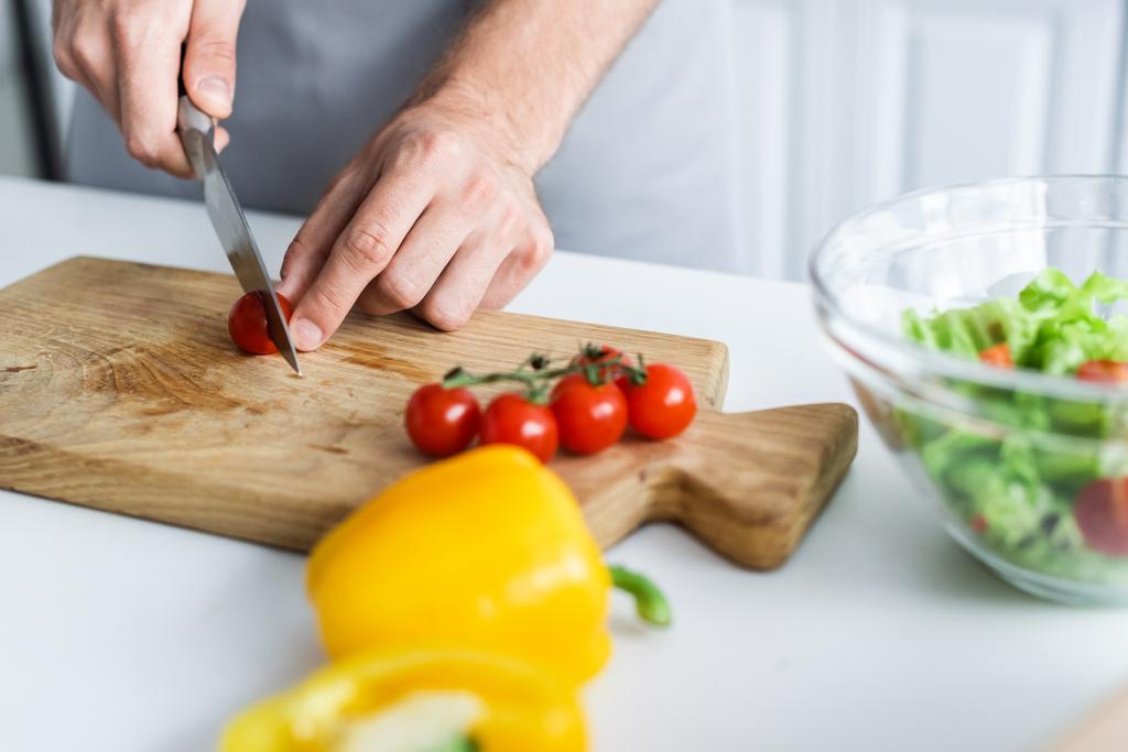 plan recadré de l'homme dans tablier de coupe tomate cerise lors de la cuisson de la salade
 - Photo, image