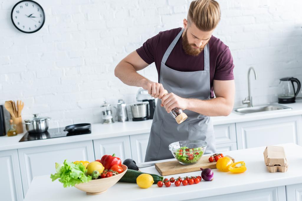 high angle view of handsome young man in apron spicing vegetable salad - Photo, Image