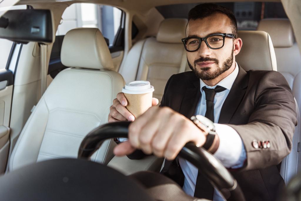 beau conducteur en costume voiture de conduite et de tenir le café dans une tasse en papier
 - Photo, image
