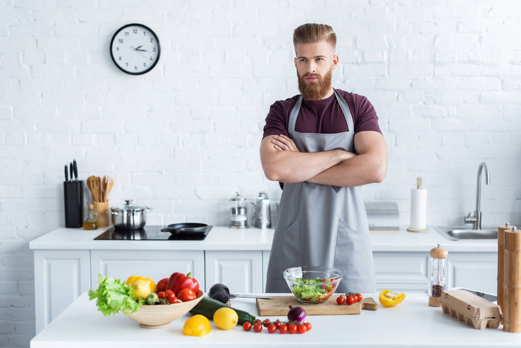 mutfakta yemek yaparken önlük ayakta çapraz kollu yakışıklı sakallı adam - Fotoğraf, Görsel