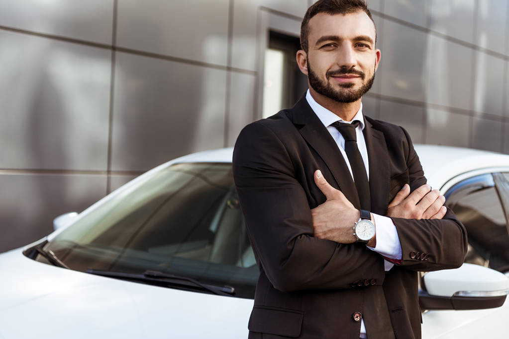 красивый улыбающийся бизнесмен, стоящий со скрещенными руками возле машины
 - Фото, изображение