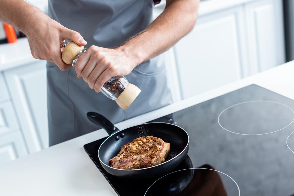 cropped shot of man holding pepper mill while cooking delicious steak in frying pan - Photo, Image