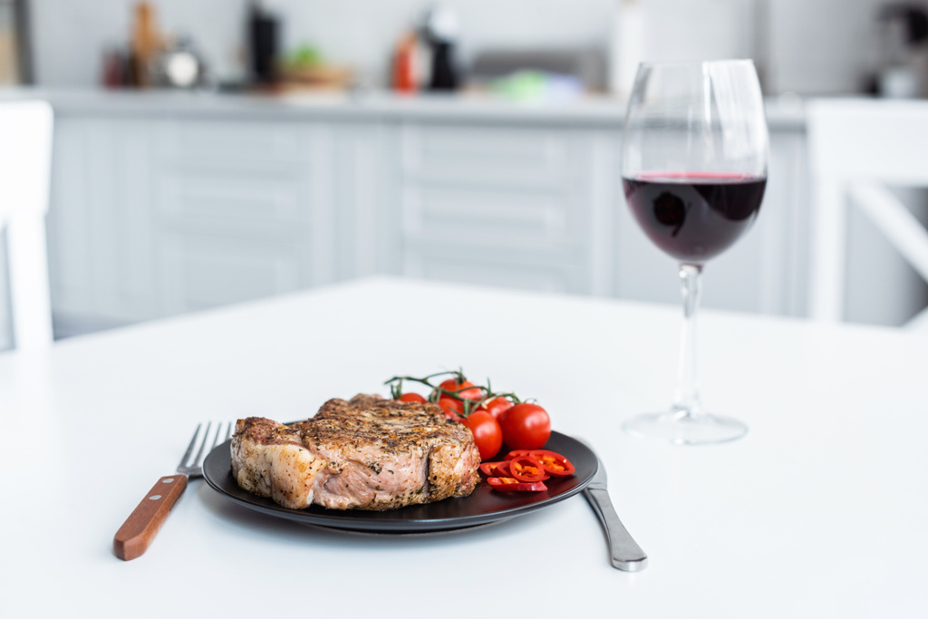 delicioso bife com tomate cereja no prato e copo de vinho tinto na mesa
 - Foto, Imagem