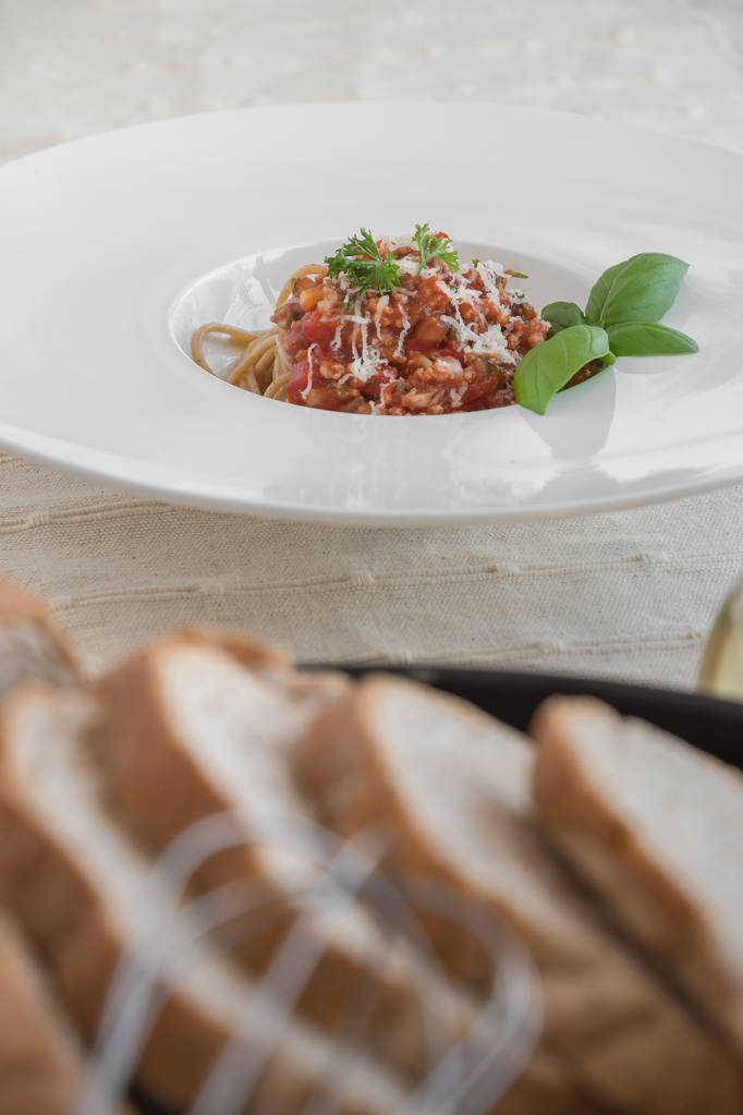 Food composition of spaghetti topped with delicious bolognaise sauce and basil served on table - Photo, Image