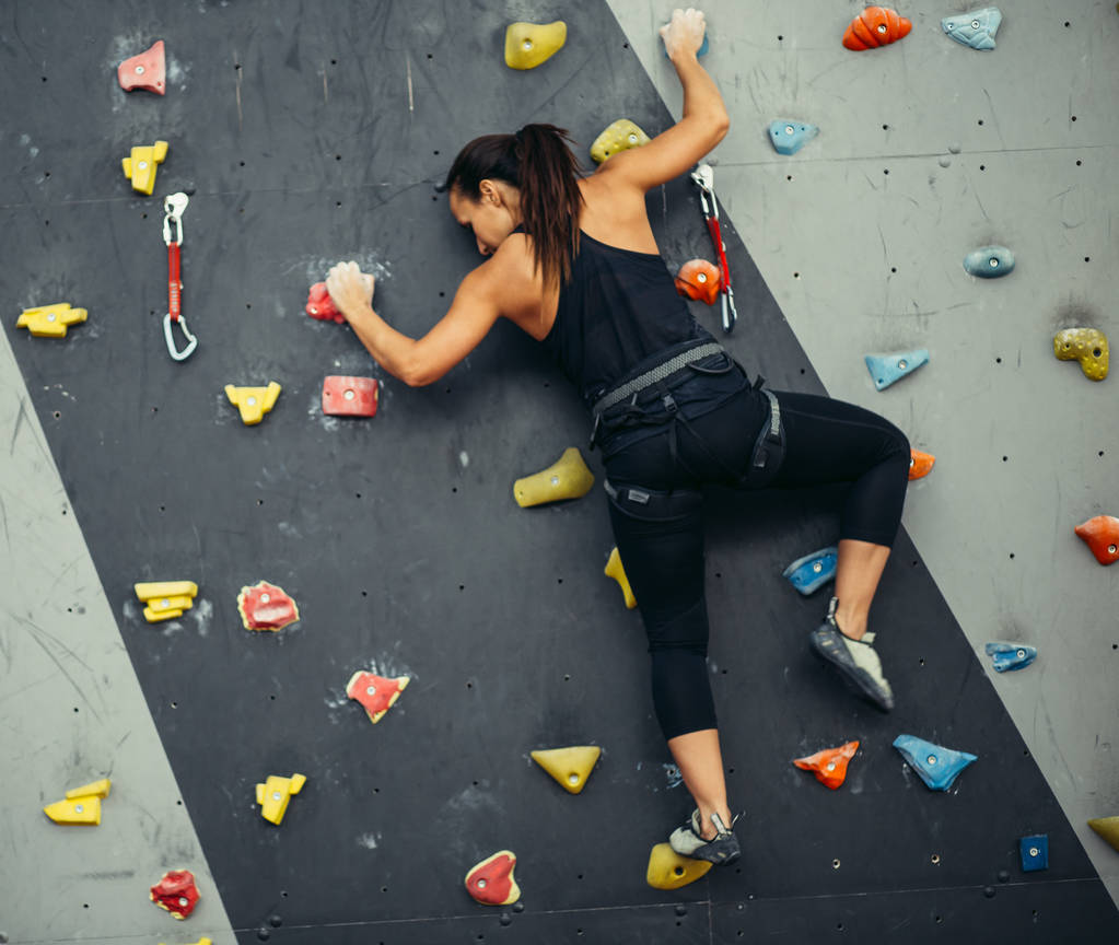 Vista trasera de una mujer irreconocible practicando escalada en roca artificial en el gimnasio. Estilo de vida activo y concepto de bouldering
. - Foto, imagen