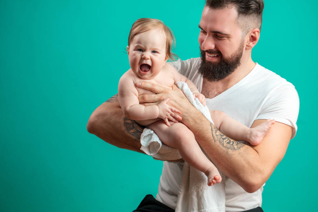 Oynak babası onun gülümseyen bebek çocuk boynuna mavi arka plan üzerinde taşıyor. - Fotoğraf, Görsel
