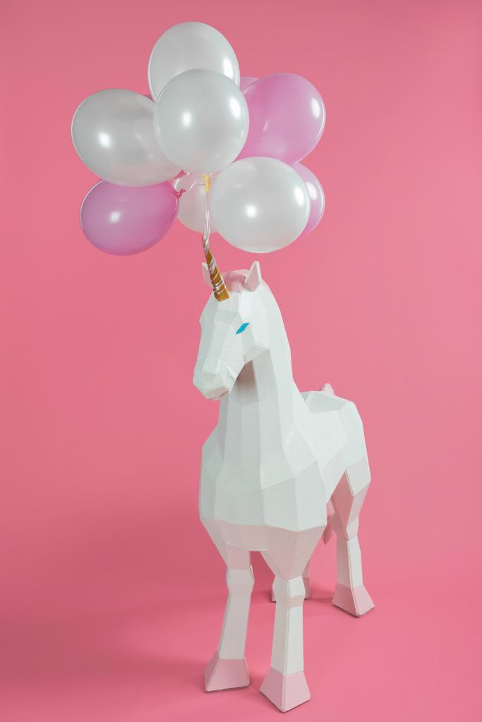 Speelgoed unicorn onder roze en witte ballonnen op roze achtergrond - Foto, afbeelding