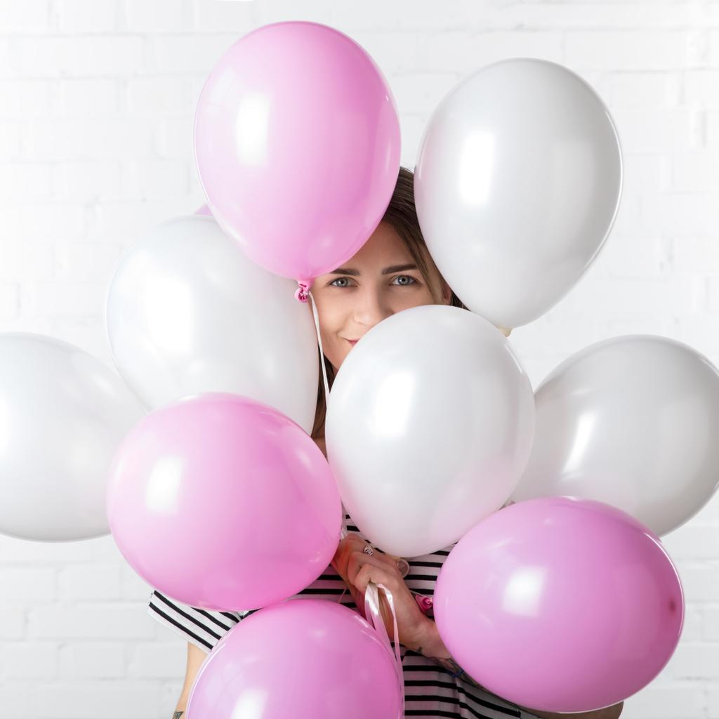 Веселая девушка позирует среди воздушных шаров на фоне стены из белого кирпича
 - Фото, изображение