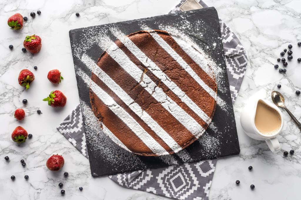 вид на вкусный домашний коричневый торт с сахарным порошком и свежими ягодами на мраморной поверхности
  - Фото, изображение
