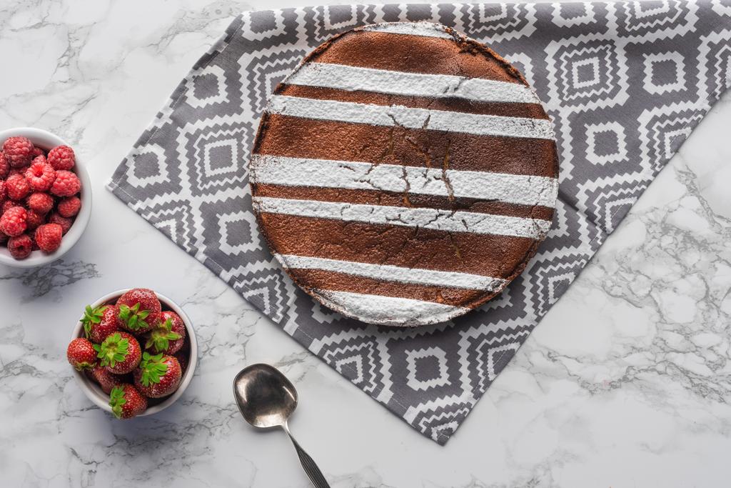 Draufsicht auf köstlichen braunen Kuchen mit Zuckerpuder und frischen Beeren auf Marmoroberfläche - Foto, Bild