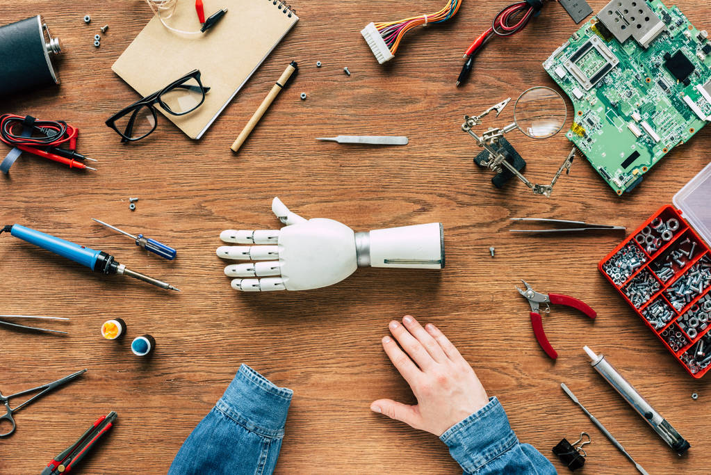 cropped image of man with amputee sitting at table with prosthetic arm surrounded by tools - Photo, Image